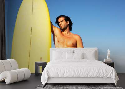 Portrait of handsome surfer with his surfboard. Young man with a surfboard on the beach. Wall mural