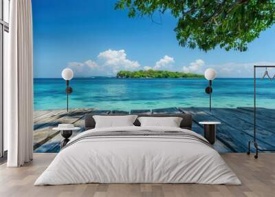 serene seascape with a weathered wooden table in the foreground framing a view of a distant tropical island crystalclear turquoise waters and a cloudless blue sky Wall mural