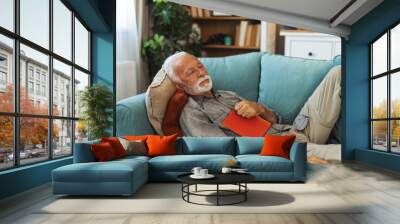 Relax, book and senior man sleeping in the living room of his modern house on a weekend. Calm, peace and elderly male person in retirement taking a nap after reading a story or novel at home. Wall mural