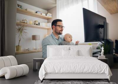 Young father working from home and babysitting his baby boy in the same time. Wall mural