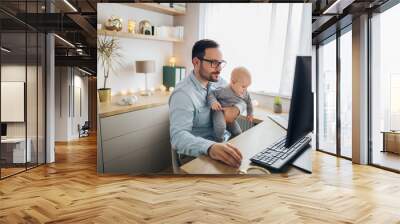 Young father working from home and babysitting his baby boy in the same time. Wall mural