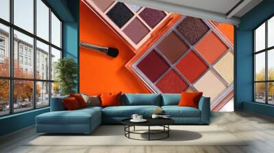 Colorful eyeshadow palettes and make up brush on orange background. Top view. Wall mural