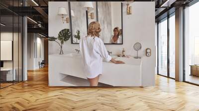 A beautiful young girl in the bathroom is standing in front of a mirror in a white shirt. Wall mural