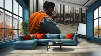 back view of a prisoner in orange suit sitting at table with and watching laptop prison cells with metal bars, generative AI Wall mural