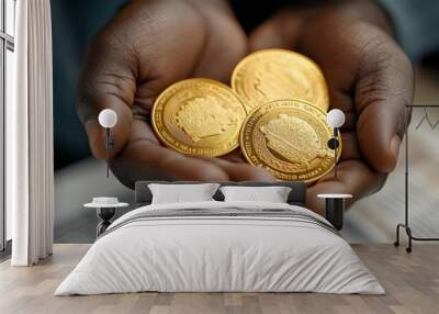 Three shiny gold coins are held in two hands, showcasing their intricate designs against a blurred background. Wall mural