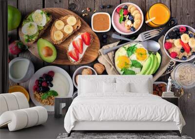 Healthy breakfast table scene with fruit, yogurts, oatmeal, smoothie, nutritious toasts and egg skillet. Top view over a wood background. Wall mural