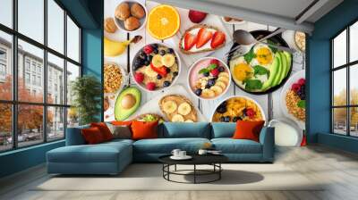 Healthy breakfast table scene with fruit, yogurts, oatmeal, smoothie bowl, cereal, nutritious toasts and egg skillet. Top view over a white wood background. Wall mural