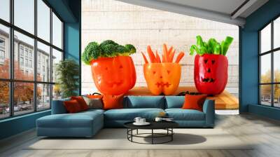 Healthy Halloween food. Vegetables for dipping in Jack o Lantern bell peppers. Scene against white wood. Wall mural