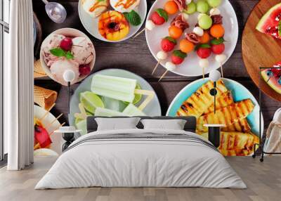 Refreshing summer food table scene. Variety of grilled fruits, ice cream and ice pops. Overhead view on a dark wood banner background. Wall mural