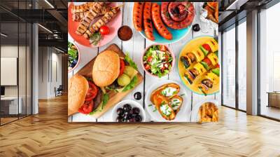 Summer BBQ or picnic food table scene. Assortment of burgers, grilled meat, vegetables, fruits, salad and potatoes. Overhead view on a white wood background. Wall mural