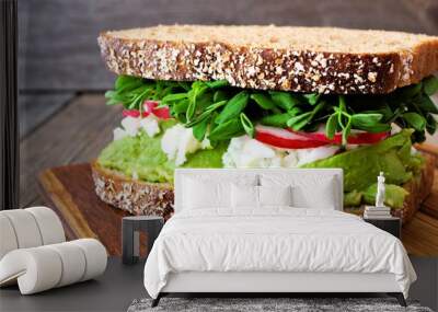 Superfood sandwich with whole grain bread, avocado, egg whites, radishes and pea shoots on wood board Wall mural