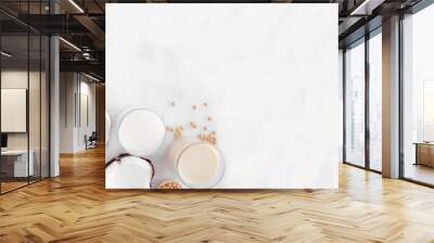 Vegan plant based non dairy milk corner border. Various types in milk bottles and glasses with scattered ingredients. Top down view over a white marble background with copy space. Wall mural