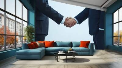 Two business professionals shake hands in a formal setting, symbolizing partnership and agreement in a corporate environment. Wall mural