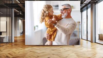 Adorable child girl and positive grandpa holding hands while dancing together in living room Wall mural