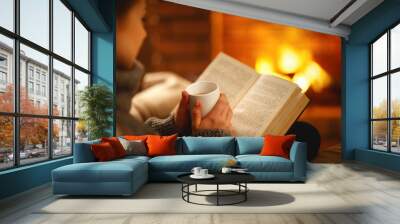 book and cup of coffee in hands of girl on  winter evening near fireplace Wall mural