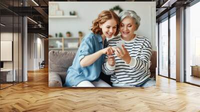 Cheerful mother and daughter using smartphone on sofa. Wall mural