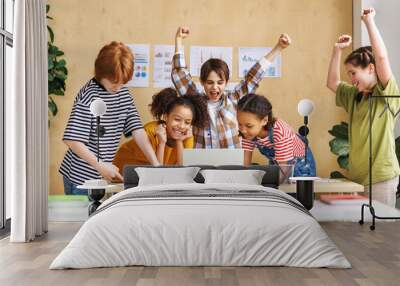 Cheerful  schoolkids   looking at laptop screen and celebrate   successful completion of collective school work   during online lesson. Wall mural