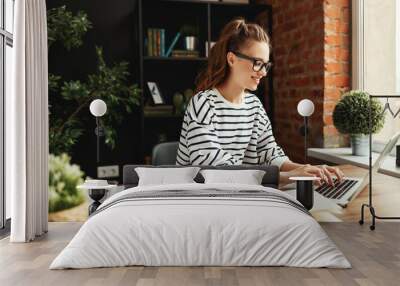 Cheerful student working on laptop at home. Wall mural