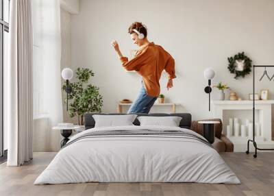 Cheerful woman listening to music and dancing on soft couch at home in day off. Wall mural