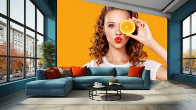 cheerful young curly woman girl with   orange   on  yellow   background. Wall mural