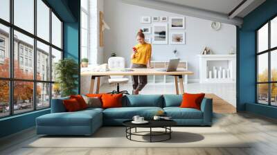 creative young woman designer in a yellow sweater in the workplace at home in interior of  apartment with large windows. Wall mural