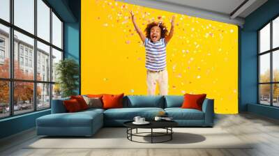 Excited African American kid jumping and catching confetti in studio Wall mural