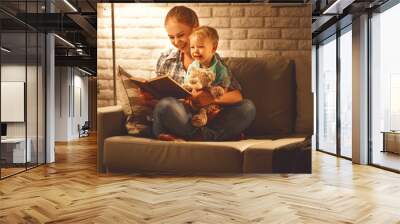 Family before going to bed mother reads to her baby son book near a lamp in the evening. Wall mural