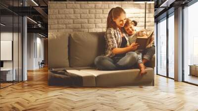 Family before going to bed mother reads to her child daughter book near a lamp in the evening Wall mural