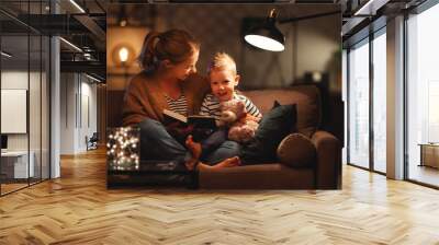 Family before going to bed mother reads to her child son book near a lamp in the evening. Wall mural