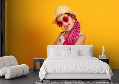 Funny happy child girl in summer dress, pink glasses and hat is laughing on yellow background Wall mural