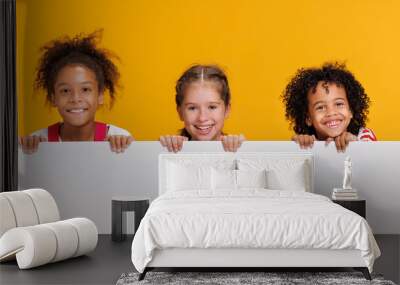 Group of cheerful happy multinational children with blank white poster on  yellow background Wall mural