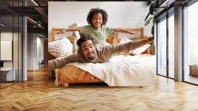 Happy african american family father and son in flying pose lying on bed at home Wall mural