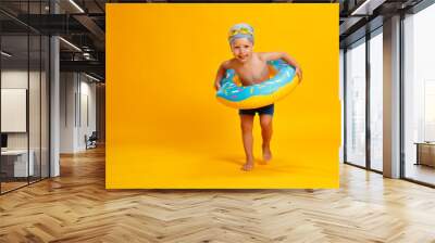 happy child boy in swimsuit with swimming ring donut on colored yellow background. Wall mural