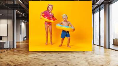 happy children girl and boy in swimsuit with swimming ring donut on colored yellow background. Wall mural