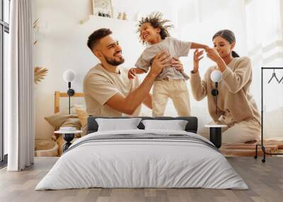 happy diverse family mom, dad and child  laughing, playing and jumping   in bed   at home. Wall mural