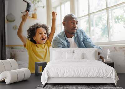 Happy ethnic family father and son playing video game console at home. Wall mural