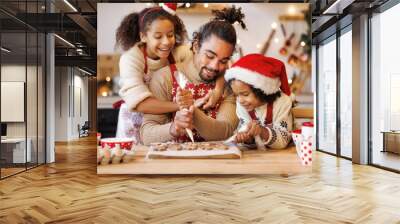 Happy ethnic family father and two kids in festive outfit making Christmas cookies together in kitchen Wall mural