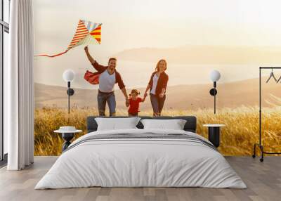 Happy family father,  mother and child daughter launch a kite on nature at sunset Wall mural