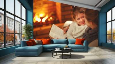 happy family mother and child daughter read book on winter evening near fireplace. Wall mural