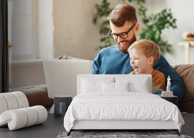 Happy father and son using laptop on sofa. Wall mural