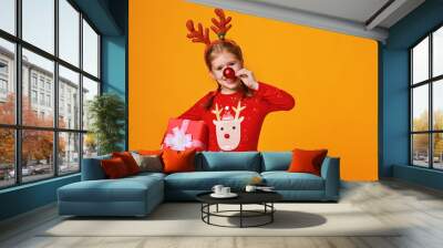 happy funny child girl in red Christmas reindeer costume with gift on yellow   background. Wall mural