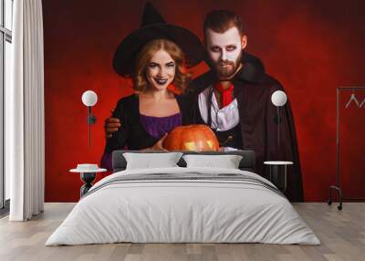 happy Halloween!  couple man and woman  in a Dracula vampire and witch costumes  with  pumpkin on  glowing red background. Wall mural