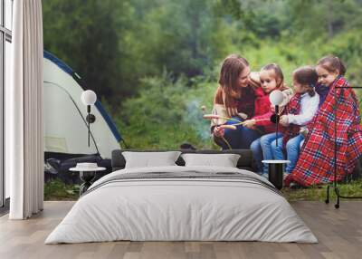 Happy tourist family on journey hike. mother and children fry sausages on bonfire near tent Wall mural