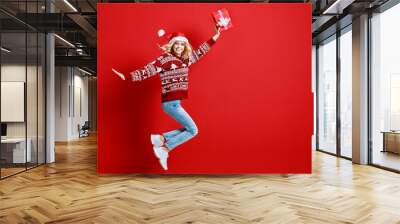 happy young cheerful girl laughs and jumps in christmas hat and with  gift on  red   background Wall mural