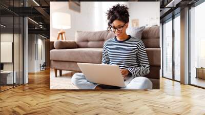 Joyful relaxed ethnic woman using laptop with interest at home Wall mural