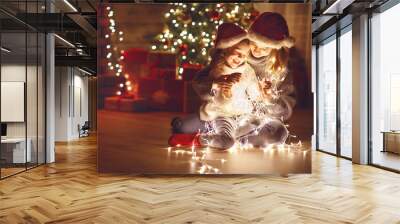 Merry Christmas! mother and child daughter with glowing garland near tree Wall mural