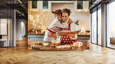 Mother and little son reading recipe book while making dough for christmas gingerbread cookies Wall mural