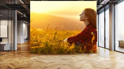 Woman sits with her back in the field and look sunset in the mountains Wall mural