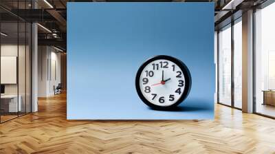 black alarm clock isolated on blue background. the clock set at 2 o'clock. Wall mural