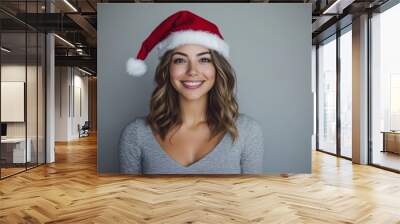 a happy woman wearing a red santa hat, posing with her hands by her sides, in front of a clean and simple background with plenty of room for text Wall mural